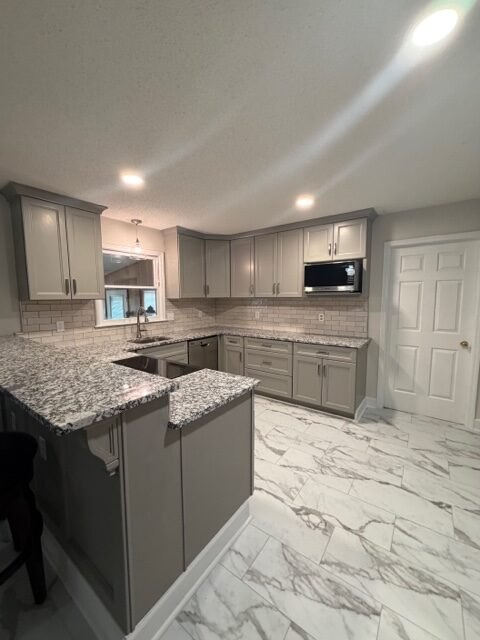 Kitchen with gray shaker cabinets, granite counters and marble look tile